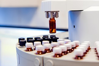Automated liquid dispenser with a robotic arm filling brown glass vials.
